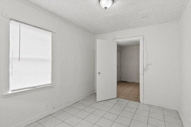 empty room featuring baseboards, a textured ceiling, and light tile patterned flooring