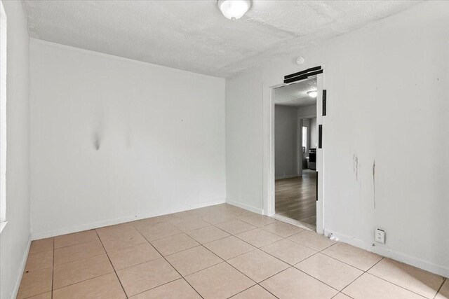 unfurnished room with a textured ceiling, baseboards, and light tile patterned floors