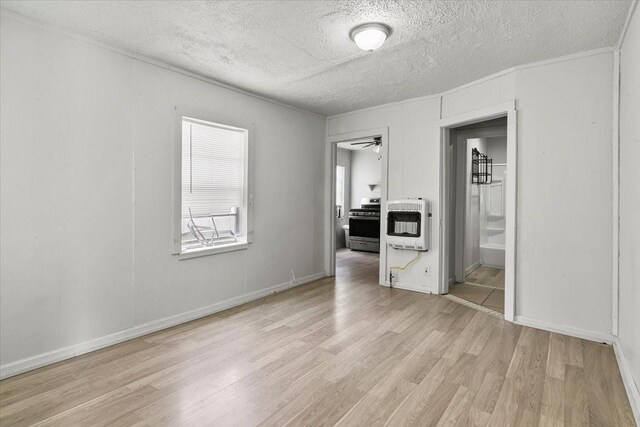 unfurnished bedroom with a textured ceiling, light wood-style flooring, baseboards, heating unit, and ensuite bath