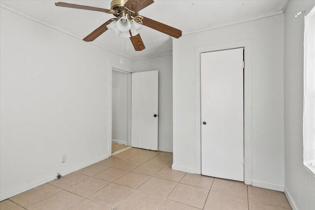 unfurnished bedroom with ornamental molding, light tile patterned flooring, baseboards, and a ceiling fan