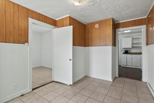 spare room with crown molding, a textured ceiling, and light tile floors