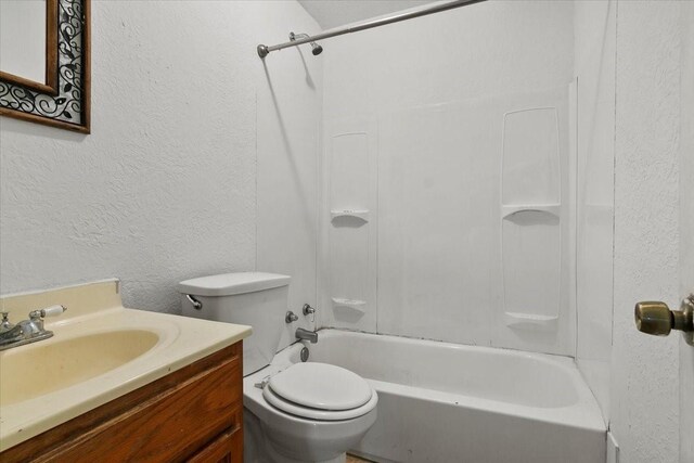 bathroom with toilet, vanity, shower / bathing tub combination, and a textured wall