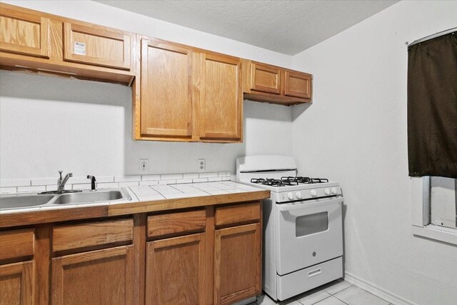 kitchen featuring white range with gas cooktop, tile counters, light tile flooring, a textured ceiling, and sink