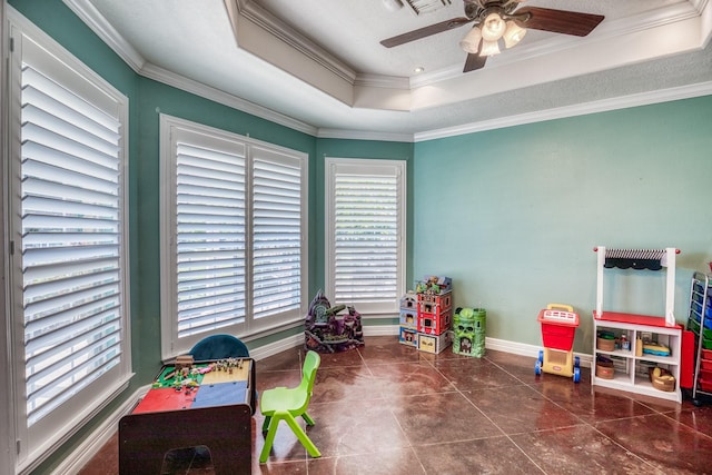 recreation room featuring dark tile patterned flooring, a textured ceiling, ornamental molding, ceiling fan, and a tray ceiling