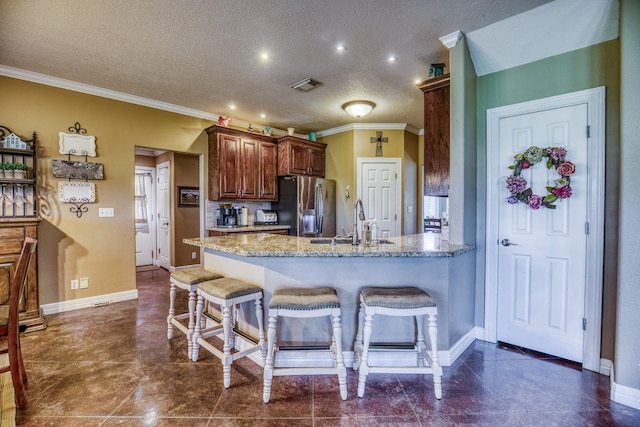 kitchen with kitchen peninsula, sink, stainless steel fridge with ice dispenser, light stone counters, and a breakfast bar area