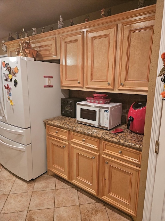 kitchen featuring light tile patterned floors, white appliances, stone countertops, and backsplash