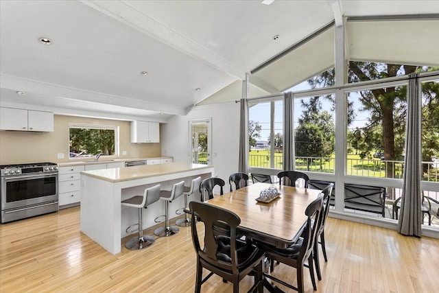 dining space featuring vaulted ceiling with beams, sink, and light hardwood / wood-style floors