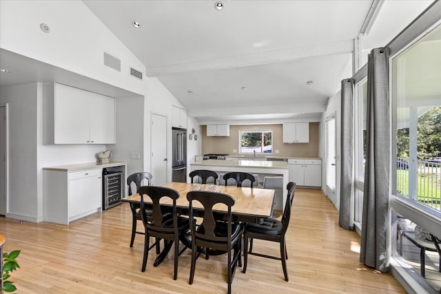 dining area featuring vaulted ceiling with beams, light hardwood / wood-style floors, and beverage cooler