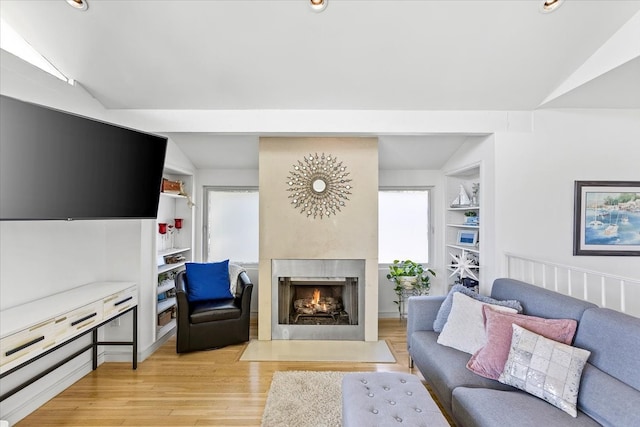 living room featuring built in features, light wood-type flooring, vaulted ceiling, and a healthy amount of sunlight