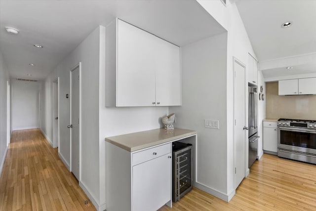 interior space featuring white cabinets, stainless steel appliances, wine cooler, and light hardwood / wood-style flooring