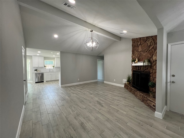 unfurnished living room featuring light hardwood / wood-style flooring, sink, a fireplace, an inviting chandelier, and lofted ceiling with beams