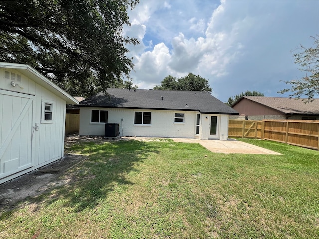 rear view of property with a lawn, a storage unit, central AC unit, and a patio