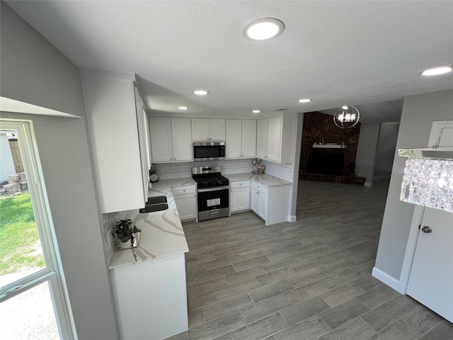 kitchen featuring a fireplace, light hardwood / wood-style flooring, decorative backsplash, stainless steel appliances, and white cabinets