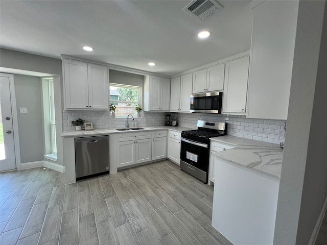 kitchen featuring backsplash, stainless steel appliances, white cabinetry, and light hardwood / wood-style flooring