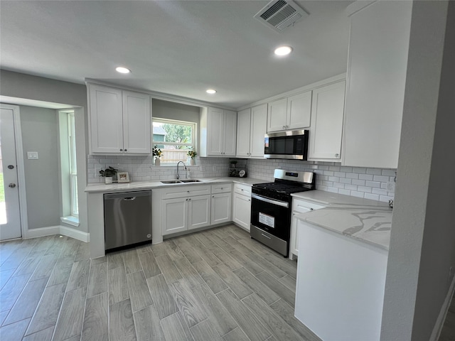 kitchen featuring backsplash, sink, light hardwood / wood-style flooring, white cabinetry, and stainless steel appliances