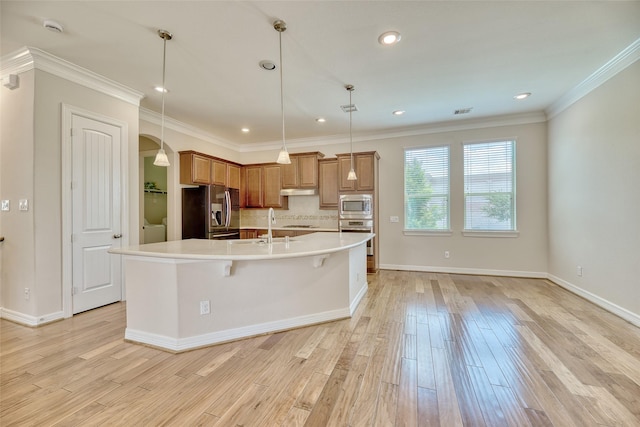 kitchen featuring appliances with stainless steel finishes, decorative light fixtures, light hardwood / wood-style flooring, and a large island with sink