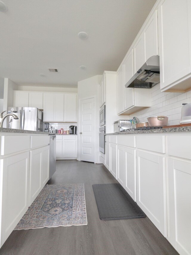 kitchen featuring stainless steel appliances, white cabinetry, wall chimney exhaust hood, decorative backsplash, and dark wood-type flooring