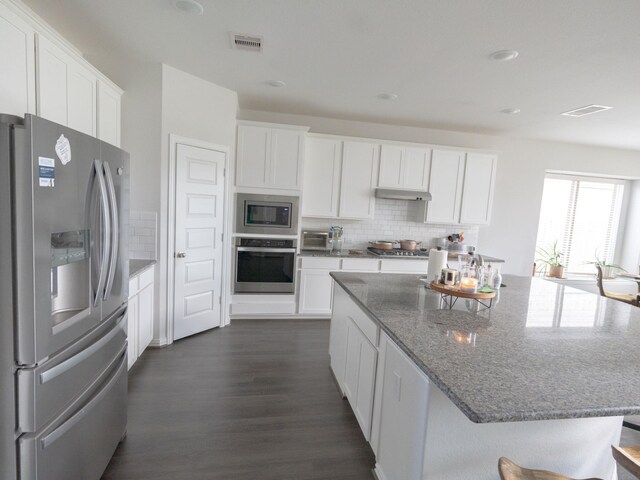 kitchen featuring appliances with stainless steel finishes, white cabinets, decorative backsplash, dark stone counters, and dark wood-type flooring