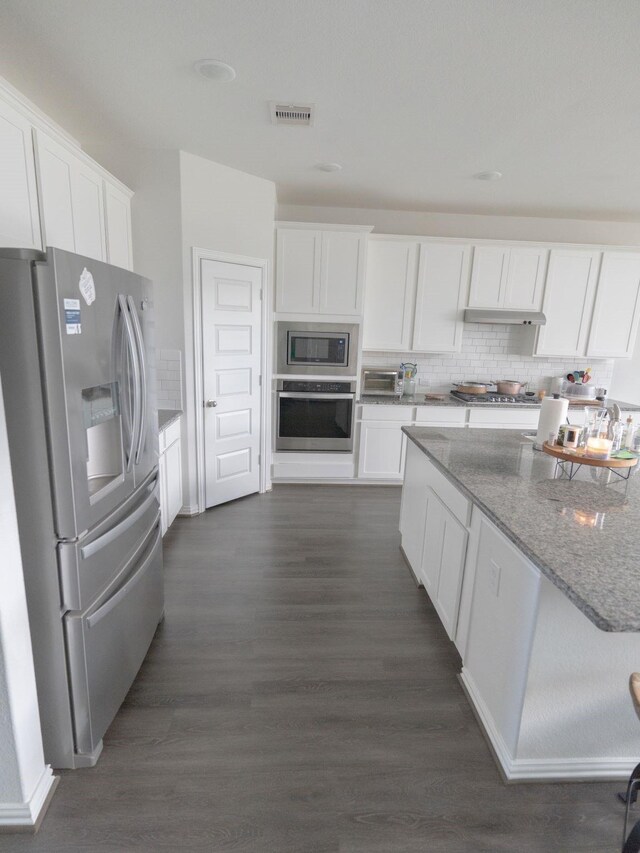 kitchen with appliances with stainless steel finishes, dark hardwood / wood-style flooring, light stone counters, white cabinets, and backsplash