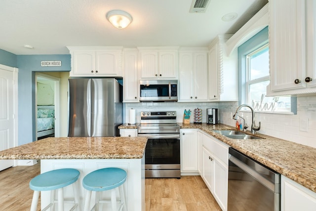 kitchen featuring sink, light stone counters, a breakfast bar, white cabinets, and appliances with stainless steel finishes