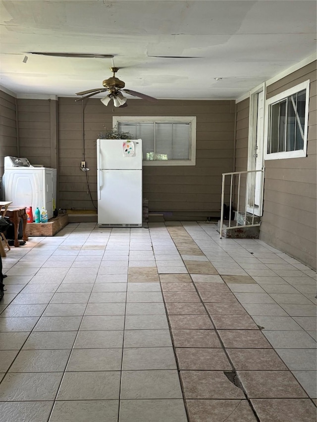 interior space featuring light tile patterned floors, wooden walls, washer and clothes dryer, and a ceiling fan