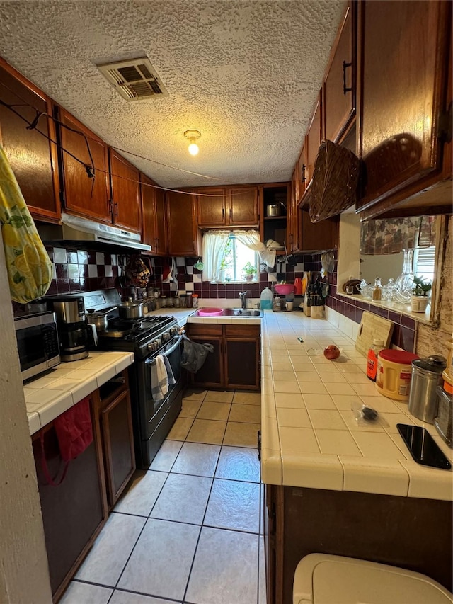 kitchen featuring tile countertops, visible vents, stainless steel microwave, black range, and under cabinet range hood