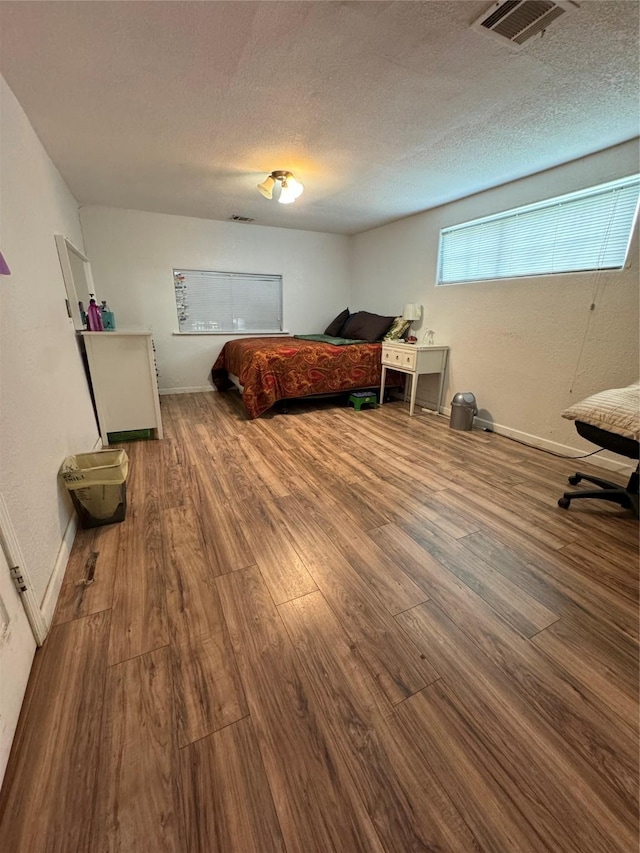 bedroom featuring visible vents, a textured ceiling, baseboards, and wood finished floors