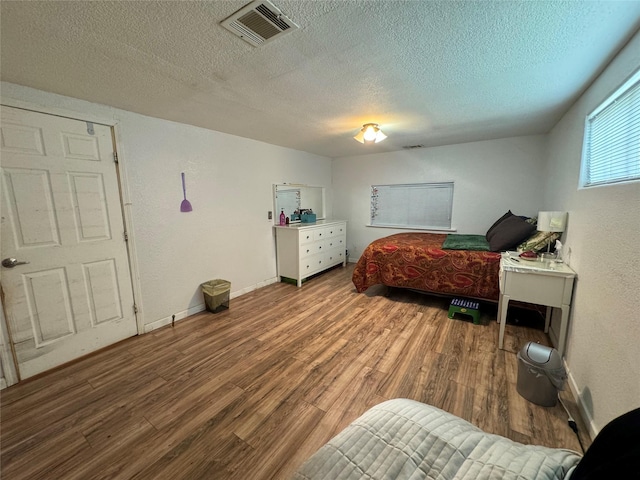 bedroom featuring visible vents, a textured wall, a textured ceiling, wood finished floors, and baseboards