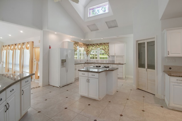 kitchen with a wealth of natural light, a center island, white cabinetry, and white fridge with ice dispenser