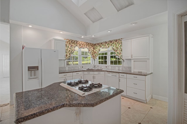 kitchen featuring white appliances, white cabinetry, a kitchen island, and dark stone countertops