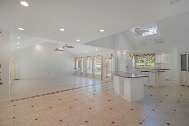 kitchen featuring high vaulted ceiling, ceiling fan, white fridge with ice dispenser, a kitchen island, and white cabinetry