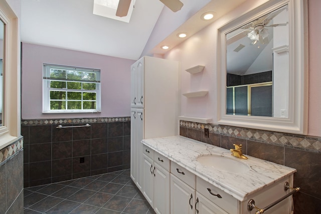 bathroom with walk in shower, tile patterned flooring, vaulted ceiling with skylight, vanity, and tile walls