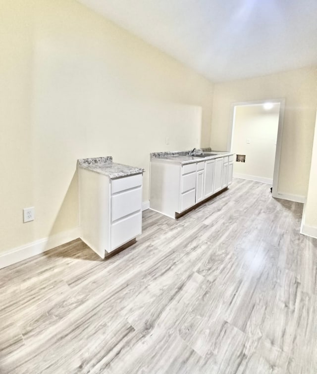 kitchen with white cabinets, light stone countertops, sink, and light hardwood / wood-style flooring