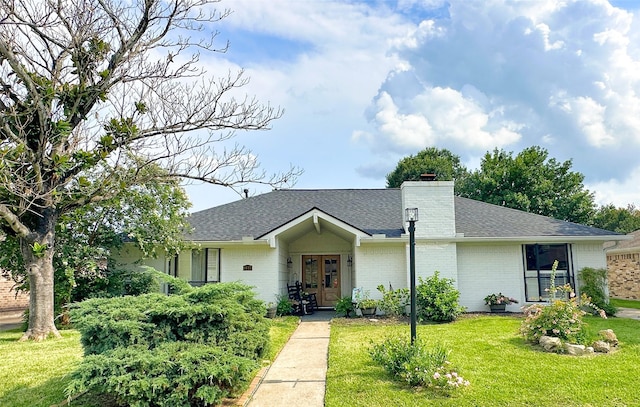 ranch-style home with brick siding, a chimney, a shingled roof, and a front lawn