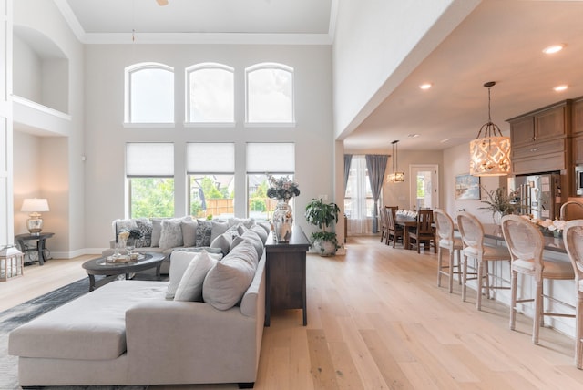 living room with a towering ceiling, light wood-type flooring, an inviting chandelier, and ornamental molding