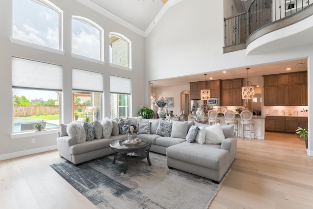 living room featuring a notable chandelier, ornamental molding, high vaulted ceiling, and light hardwood / wood-style flooring