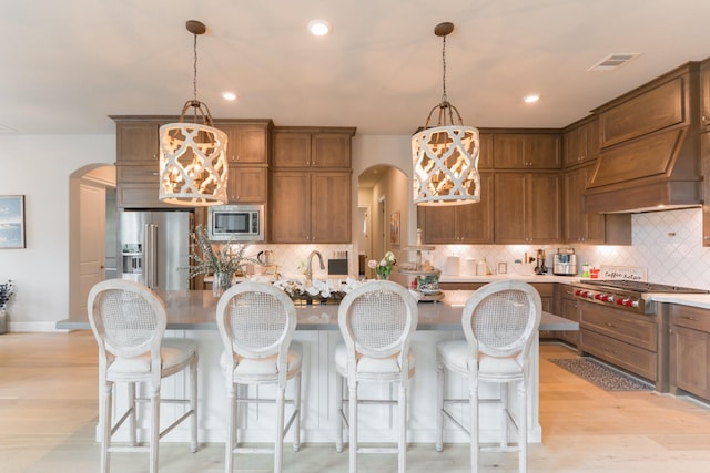 kitchen with a breakfast bar, pendant lighting, light wood-type flooring, and appliances with stainless steel finishes