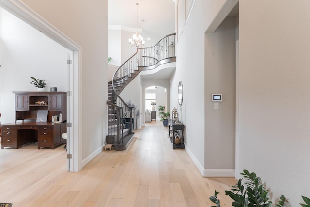 foyer with a notable chandelier, light hardwood / wood-style floors, a towering ceiling, and crown molding