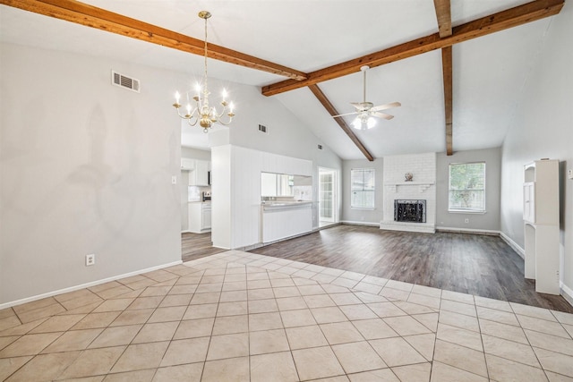 unfurnished living room with ceiling fan with notable chandelier, beam ceiling, high vaulted ceiling, and a brick fireplace