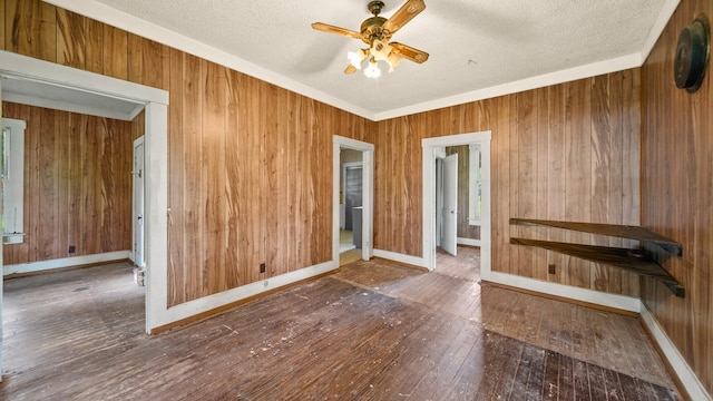 unfurnished room featuring hardwood / wood-style floors, a textured ceiling, ceiling fan, and wooden walls