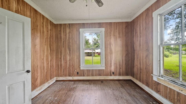 empty room with wood walls, hardwood / wood-style floors, ceiling fan, and a textured ceiling