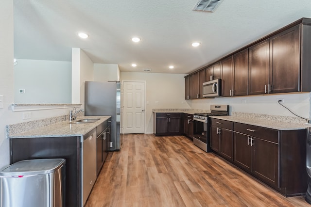 kitchen with sink, dark brown cabinetry, light wood-type flooring, appliances with stainless steel finishes, and light stone counters