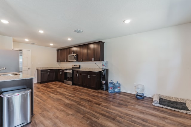 kitchen with appliances with stainless steel finishes, sink, dark brown cabinets, light stone counters, and dark hardwood / wood-style floors