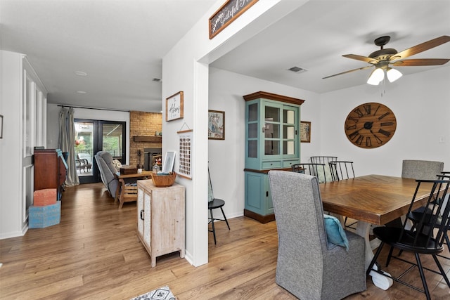 dining area featuring light hardwood / wood-style flooring, a brick fireplace, and ceiling fan