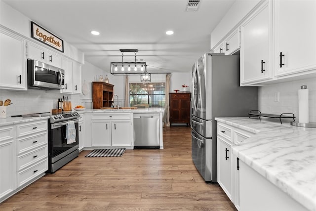 kitchen featuring stainless steel appliances, sink, pendant lighting, white cabinets, and light hardwood / wood-style floors