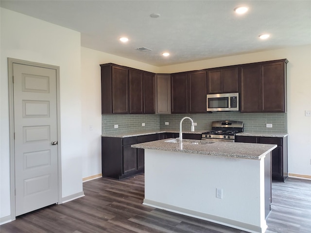 kitchen featuring dark wood finished floors, a kitchen island with sink, stainless steel appliances, dark brown cabinets, and a sink