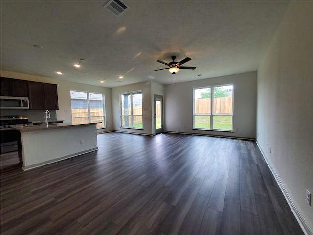 unfurnished living room with a sink, a ceiling fan, visible vents, baseboards, and dark wood finished floors