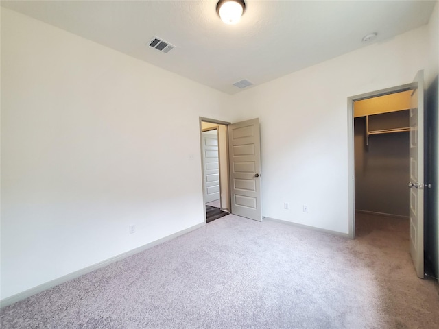 unfurnished bedroom featuring carpet flooring, visible vents, baseboards, a closet, and a walk in closet