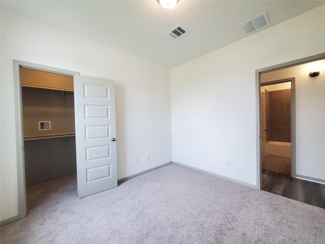 unfurnished bedroom featuring a walk in closet, visible vents, dark carpet, and baseboards