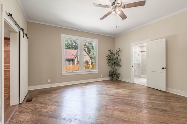 unfurnished bedroom featuring crown molding, wood-type flooring, a barn door, ensuite bathroom, and ceiling fan